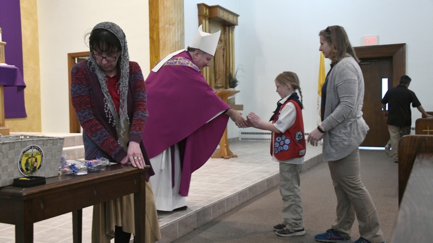  Bishop Robert J. McClory presents a Deus et Familia Mea (God and My Family) religious emblem to Tenderheart Teresa Dustin, 8, of the American Heritage Girls as her mother Mary Dustin (right) follows her and AHG troop shepherd Emily Hackett (left) prepares awards at the Gary Diocese Catholic Committee on Scouting Religious Emblem Mass on March 3 at St. Bridget church in Hobart. American Heritage Girls and Boy Scouts of America members worshipped at Mass presided over by Bishop Robert J. McClory, and later r